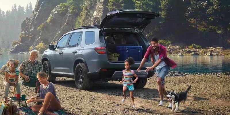 A family gathering their items from the open trunk of a gray 2024 Honda Pilot parked at a campsite