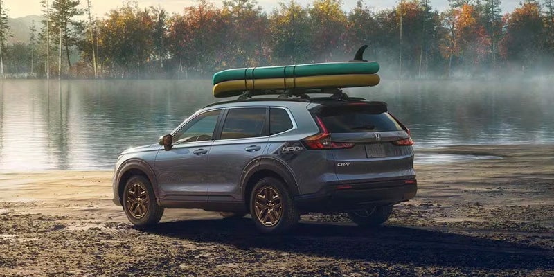 A grey 2024 Honda CR-V parked next to a small body of water with a yellow and green canoe each secured to the roof rack
