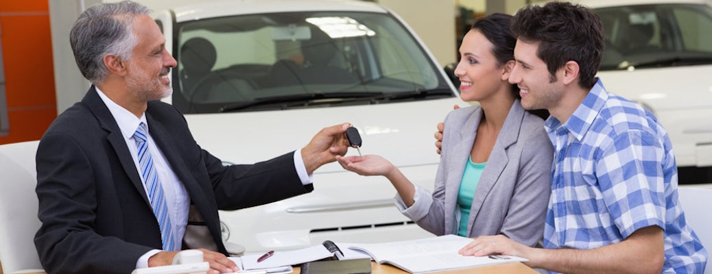 Car Sales Man handing over keys to young couple